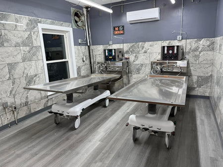 A side-by-side view of a hydraulic embalming table and a folded dressing table, emphasizing space-saving design
